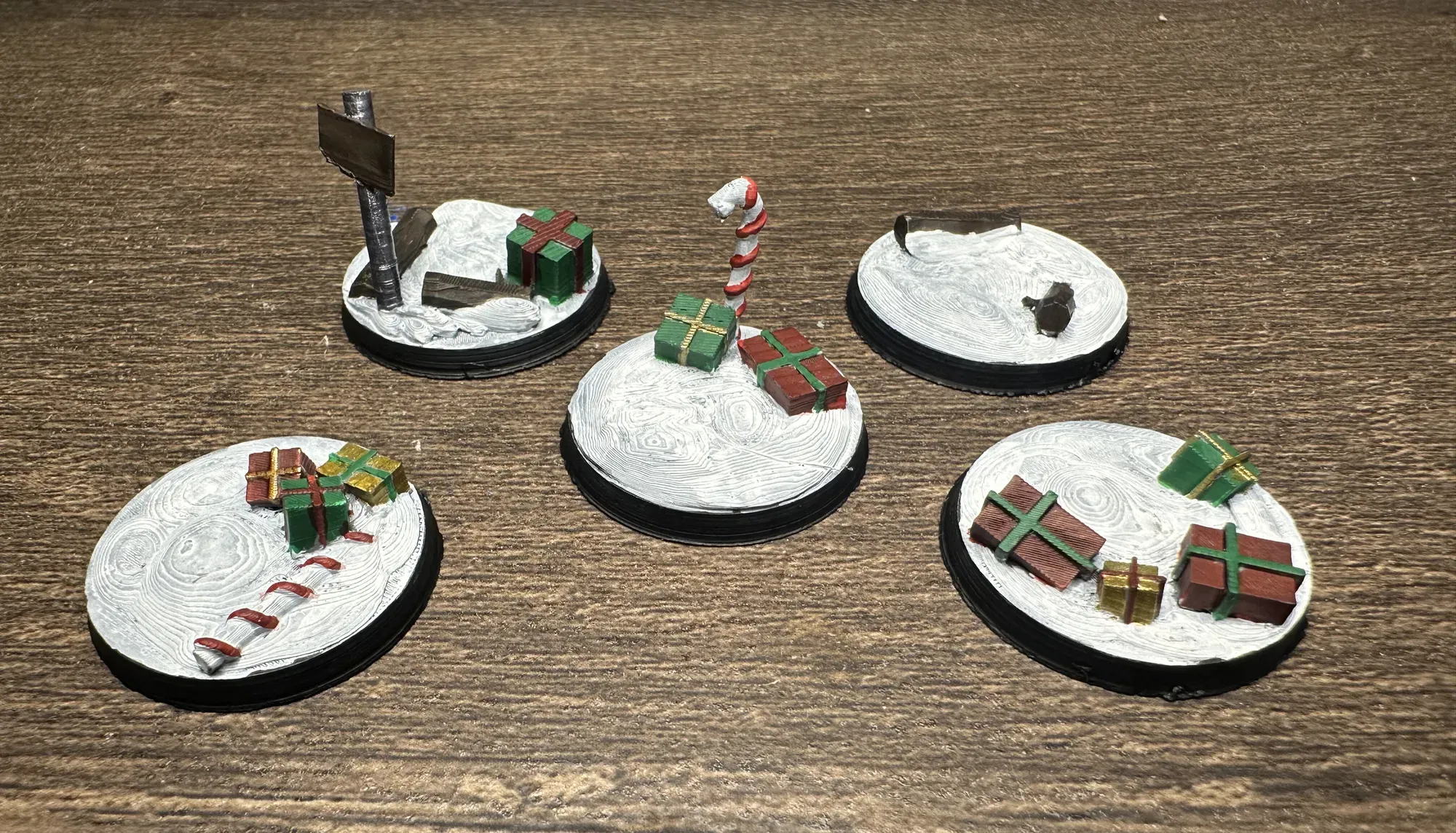 Five 28mm Christmas themed miniature bases printed and painted in red, green, and gold